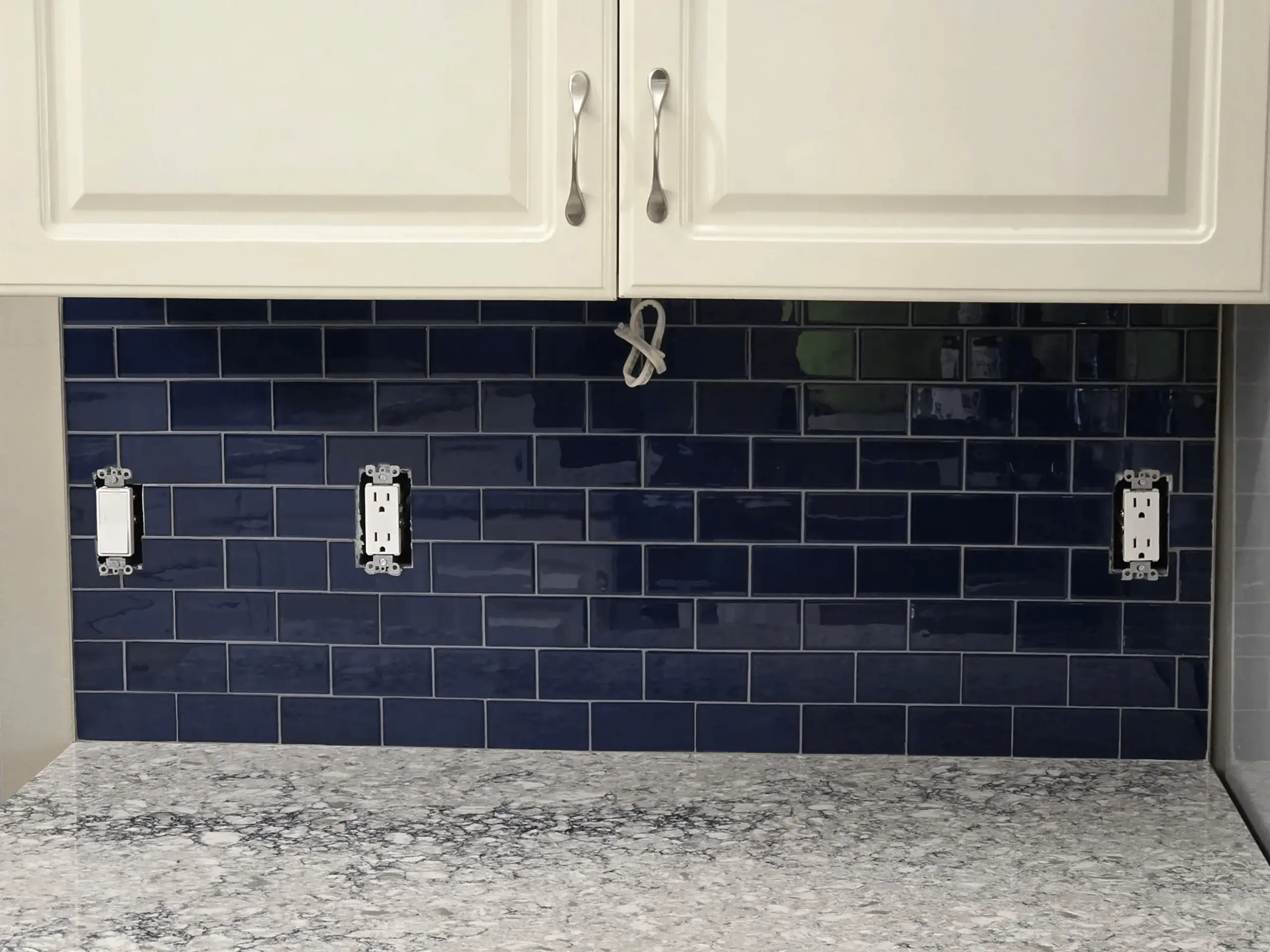 Blue tiled backsplash with white cabinets above.